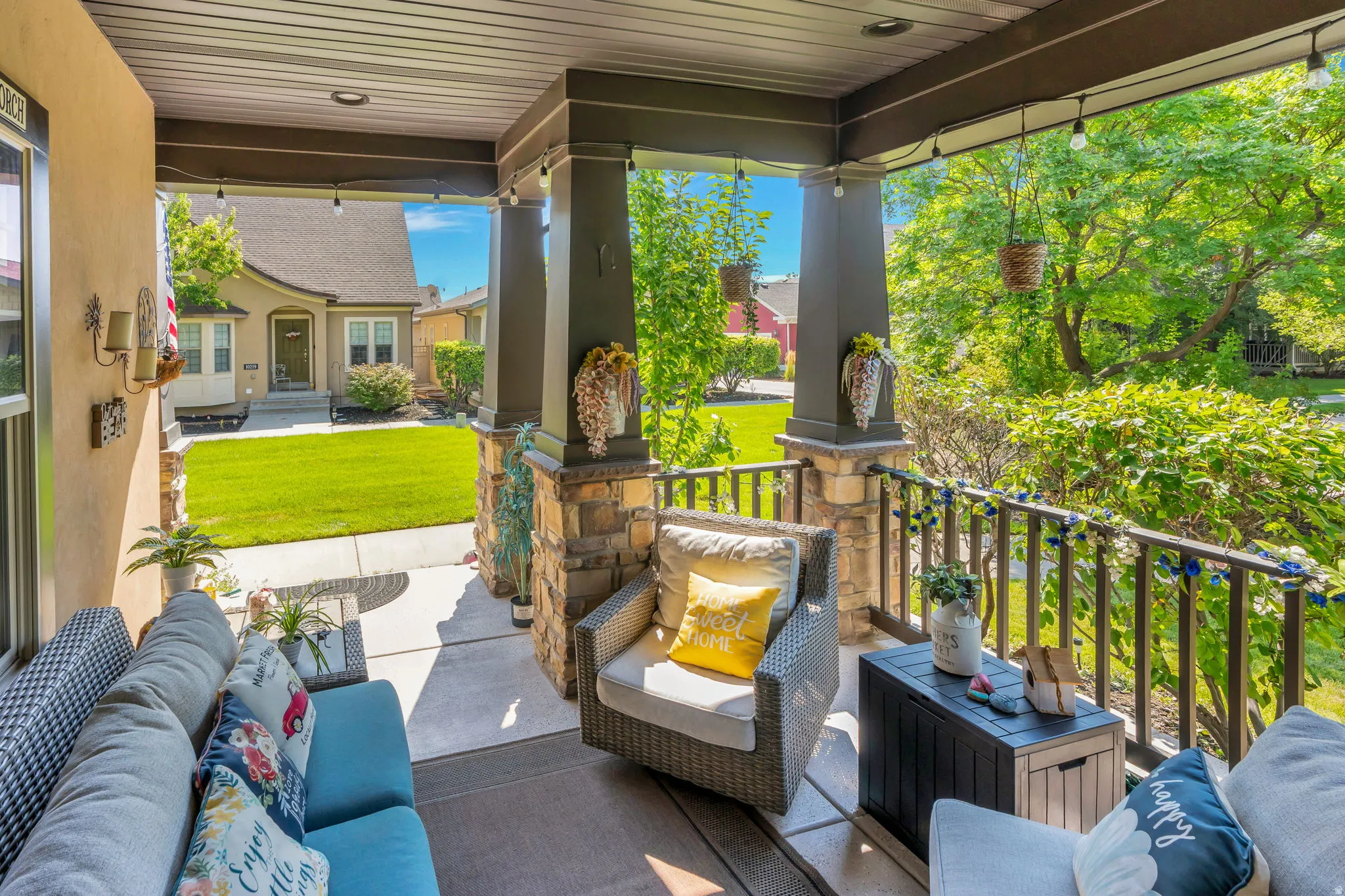 Covered front porch with stone-clad columns, a dark wood-finish ceiling, and string lighting