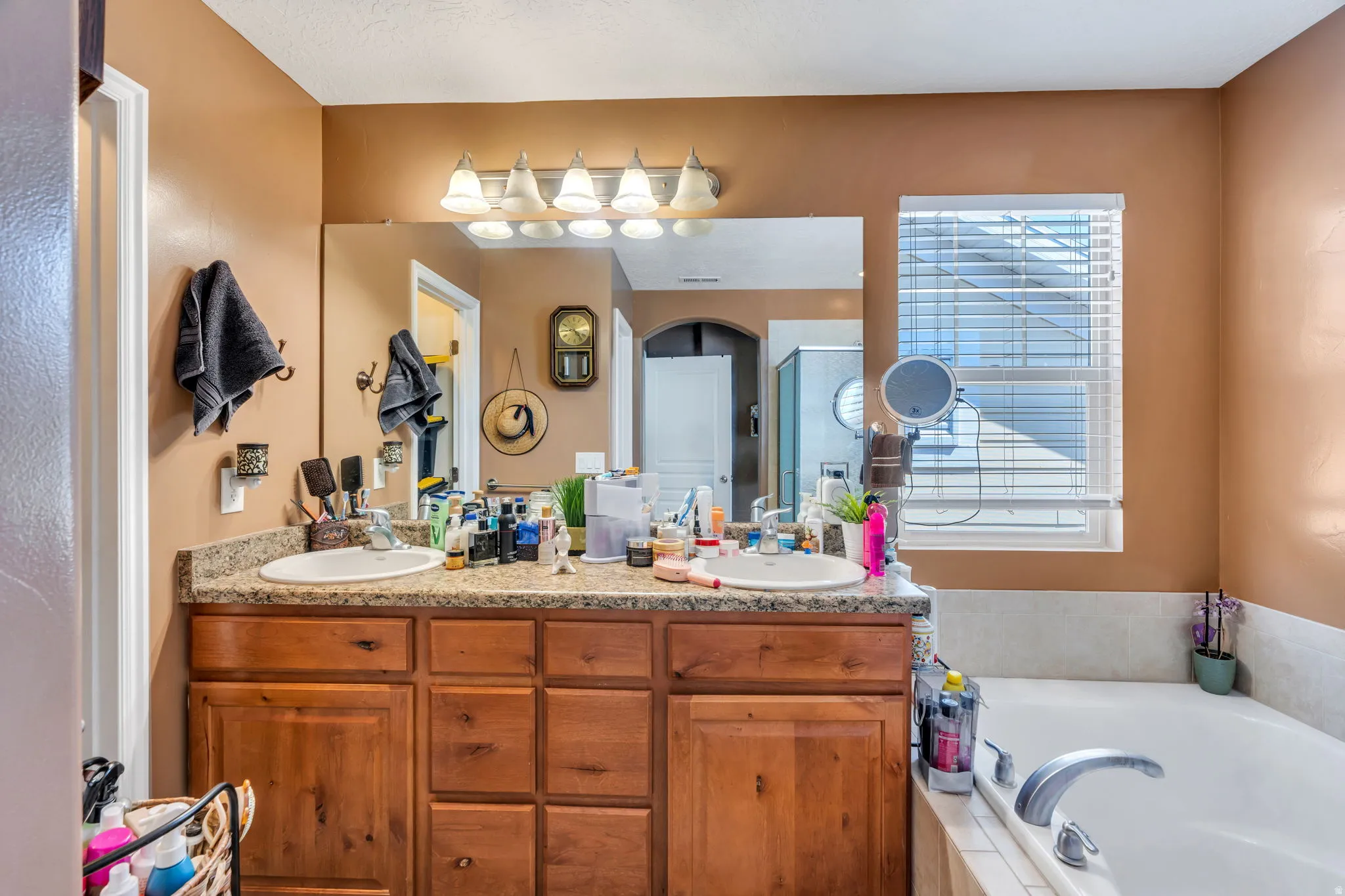 Dual vanity with wood-finish cabinetry, a large mirror, and an adjacent built-in bathtub