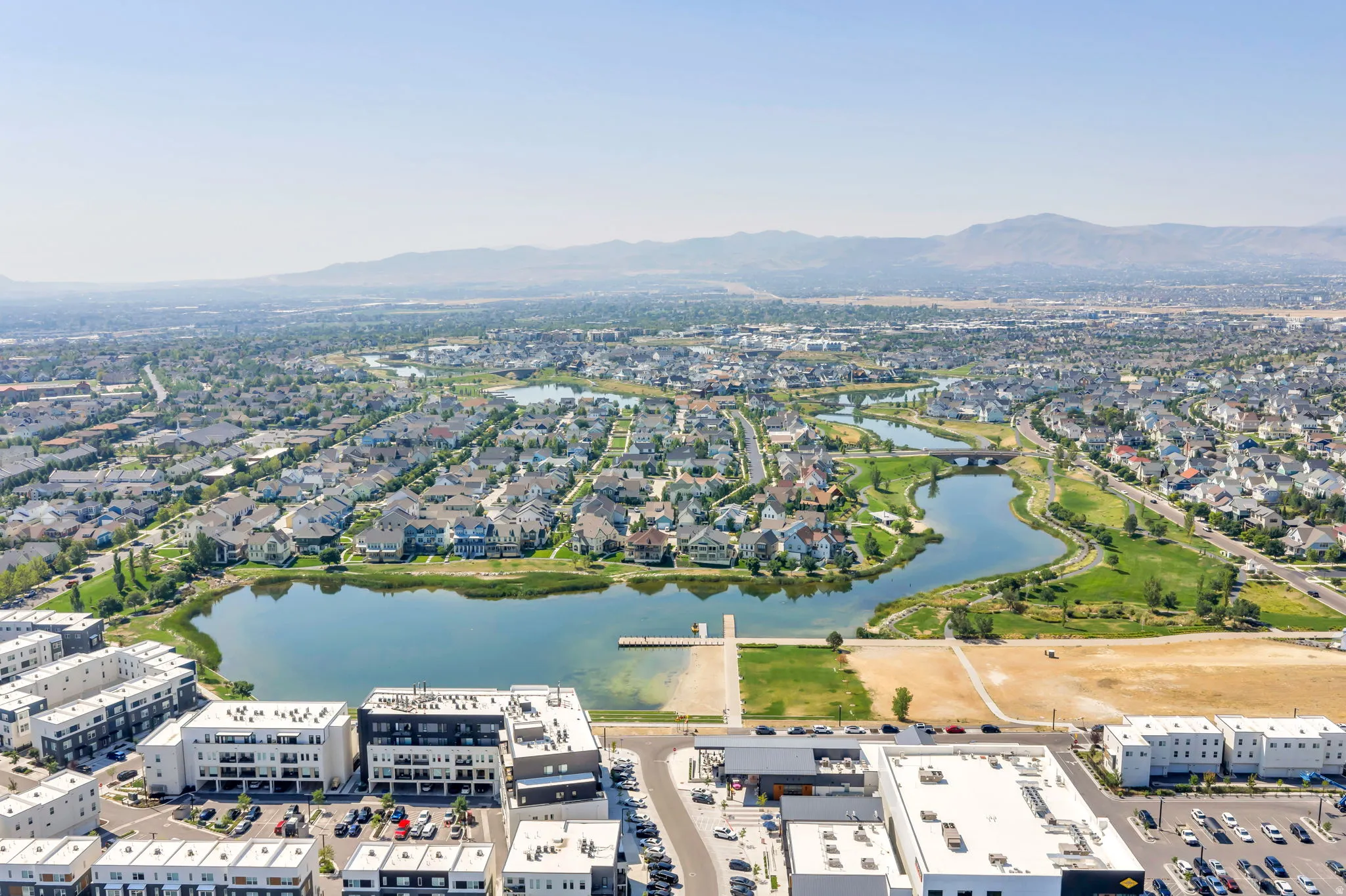 Aerial perspective showcasing a residential area with a prominent body of water, surrounding green spaces, and distant mountains
