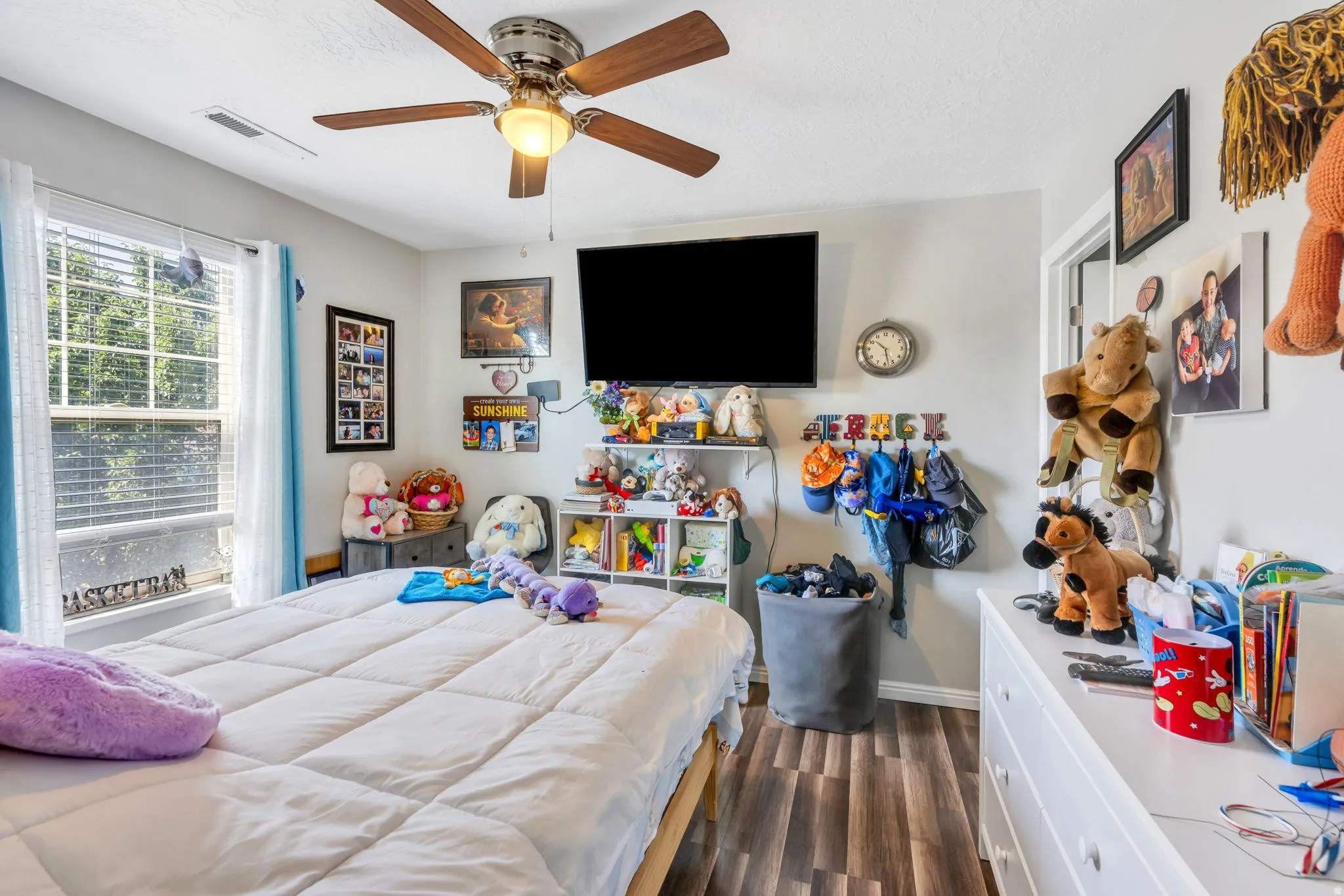 Window with exterior foliage, ceiling fan with light fixture, wood-finish flooring, white walls, and a white baseboard