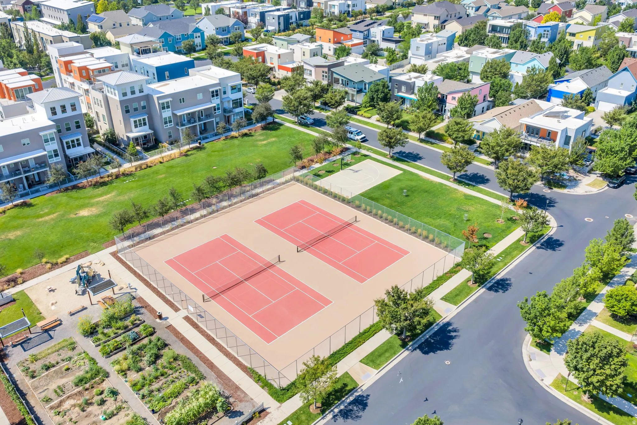 Two fenced tennis courts, basketball half-court, community garden beds, and a playground area with open green spaces