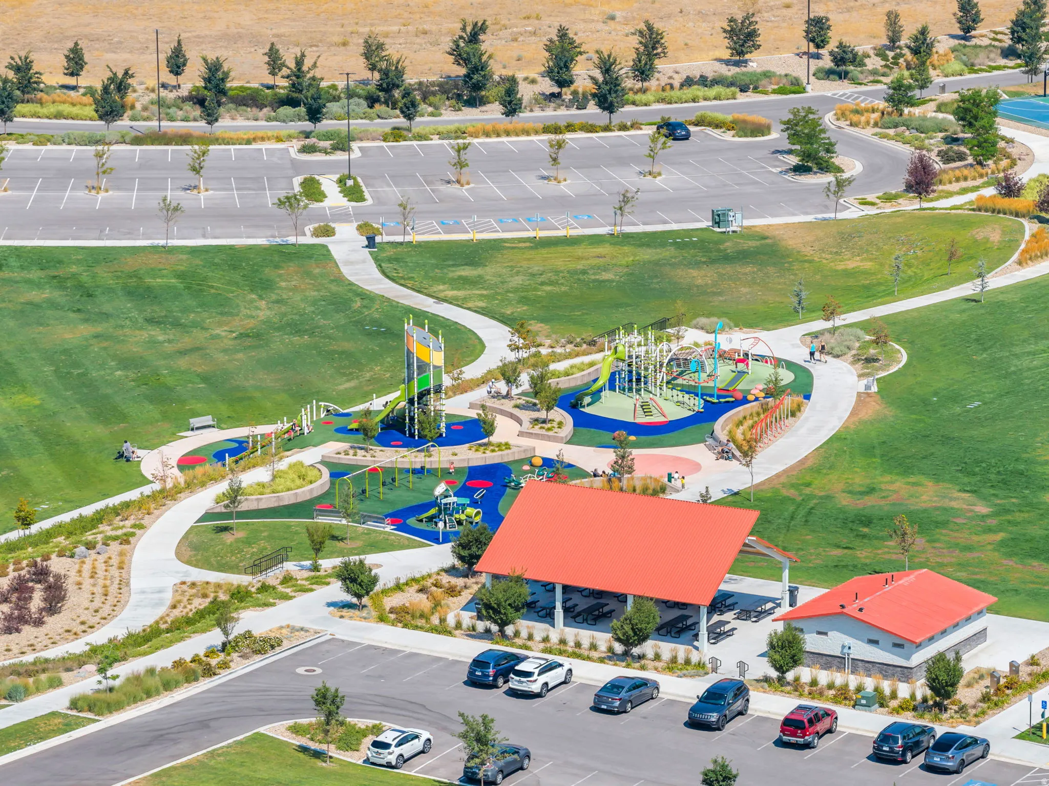 Expansive park grounds featuring multiple playground structures, paved walking paths, covered picnic areas, and ample parking