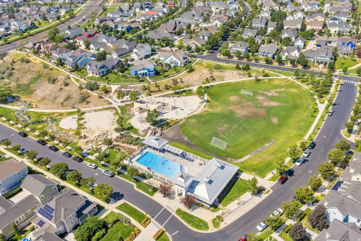 Community recreational area featuring a swimming pool, expansive green space, paved pathways, and sand play areas