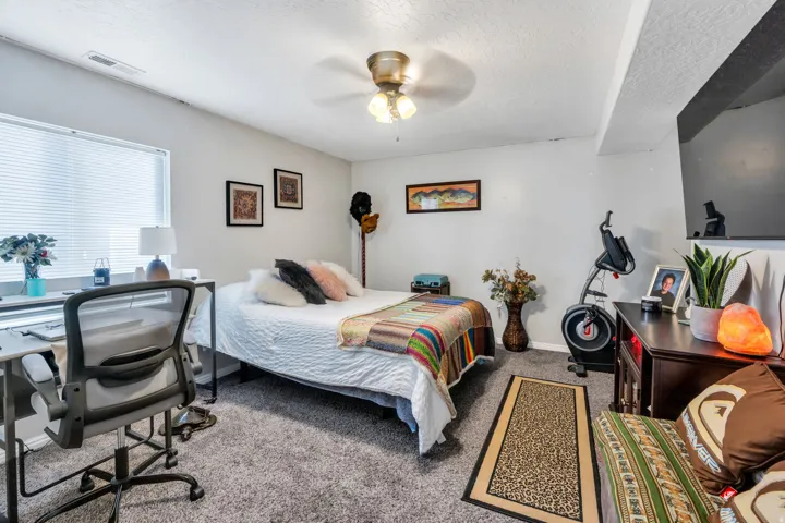 Light gray wall paint, window with horizontal blinds, ceiling fan with integrated lighting, gray carpet flooring, and a built-in wall niche