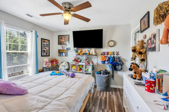 Window with exterior foliage, ceiling fan with light fixture, wood-finish flooring, white walls, and a white baseboard