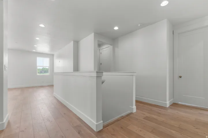 Light wood-finish flooring with white walls and trim, featuring a square window and recessed ceiling lighting