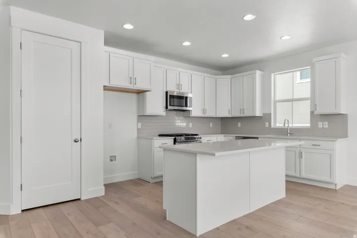 Recessed lighting illuminating a kitchen featuring a central island, white cabinetry, light countertops, and a subway tile backsplash