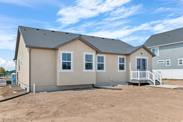 Stucco exterior with a gray shingle roof, multiple windows, a rear deck, and a sliding glass door