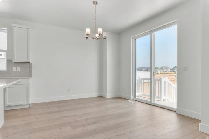 Open-concept space featuring wood-finish flooring, white cabinetry, a neutral subway tile backsplash, a modern chandelier, and sliding glass doors with an exterior deck