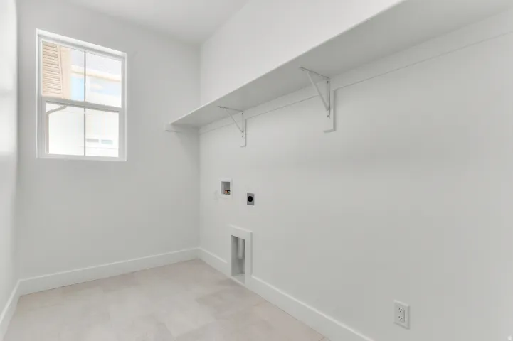 Dedicated utility room with a window, wall-mounted shelving, and light-toned tile flooring