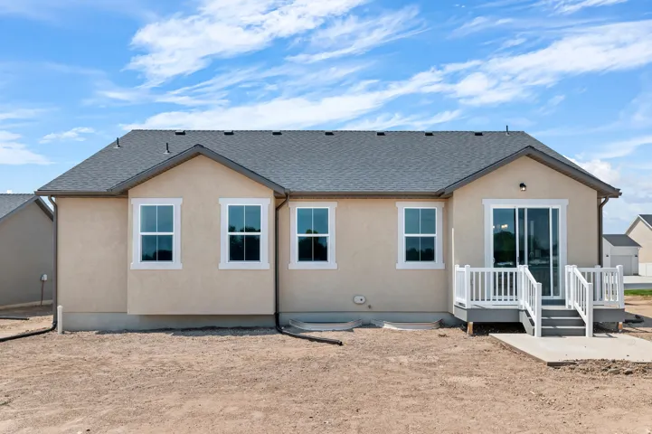 Stucco exterior with a dark shingle roof, white-framed windows, and a built-in deck with white railings and sliding glass doors