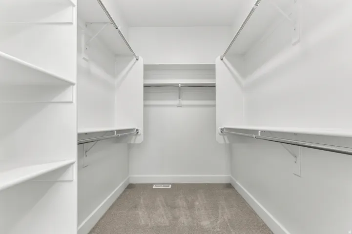 Walk-in closet featuring white built-in shelving, multiple hanging rods, and light-toned carpeting