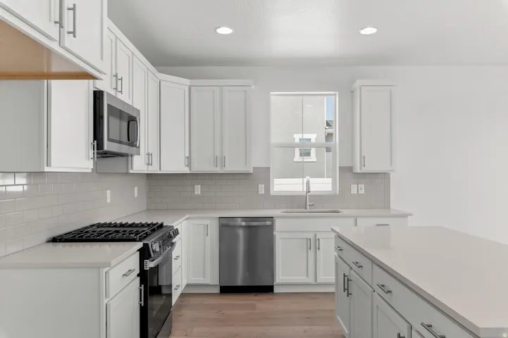 Kitchen featuring white shaker cabinetry, stainless steel appliances, light-toned countertops, subway tile backsplash, and wood-finish flooring