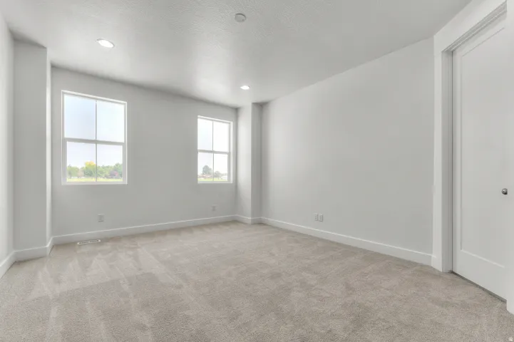Expansive room featuring light-toned carpeting, two windows with white frames, and recessed ceiling lighting