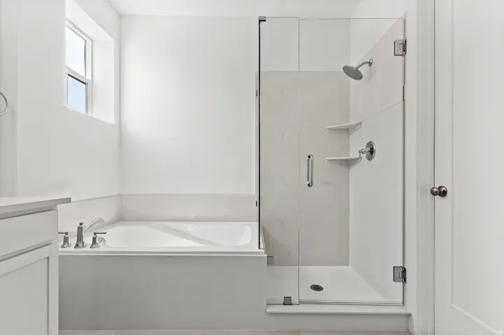 Built-in soaking tub with deck-mounted fixtures, separate walk-in shower with glass enclosure, integrated shower shelving, and upper window