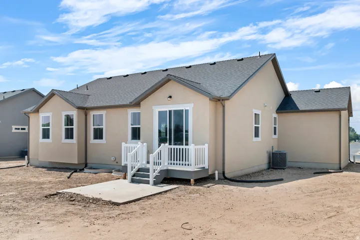 Stucco exterior with a dark shingle roof, featuring a raised deck with white railings, a sliding glass door, and a concrete patio