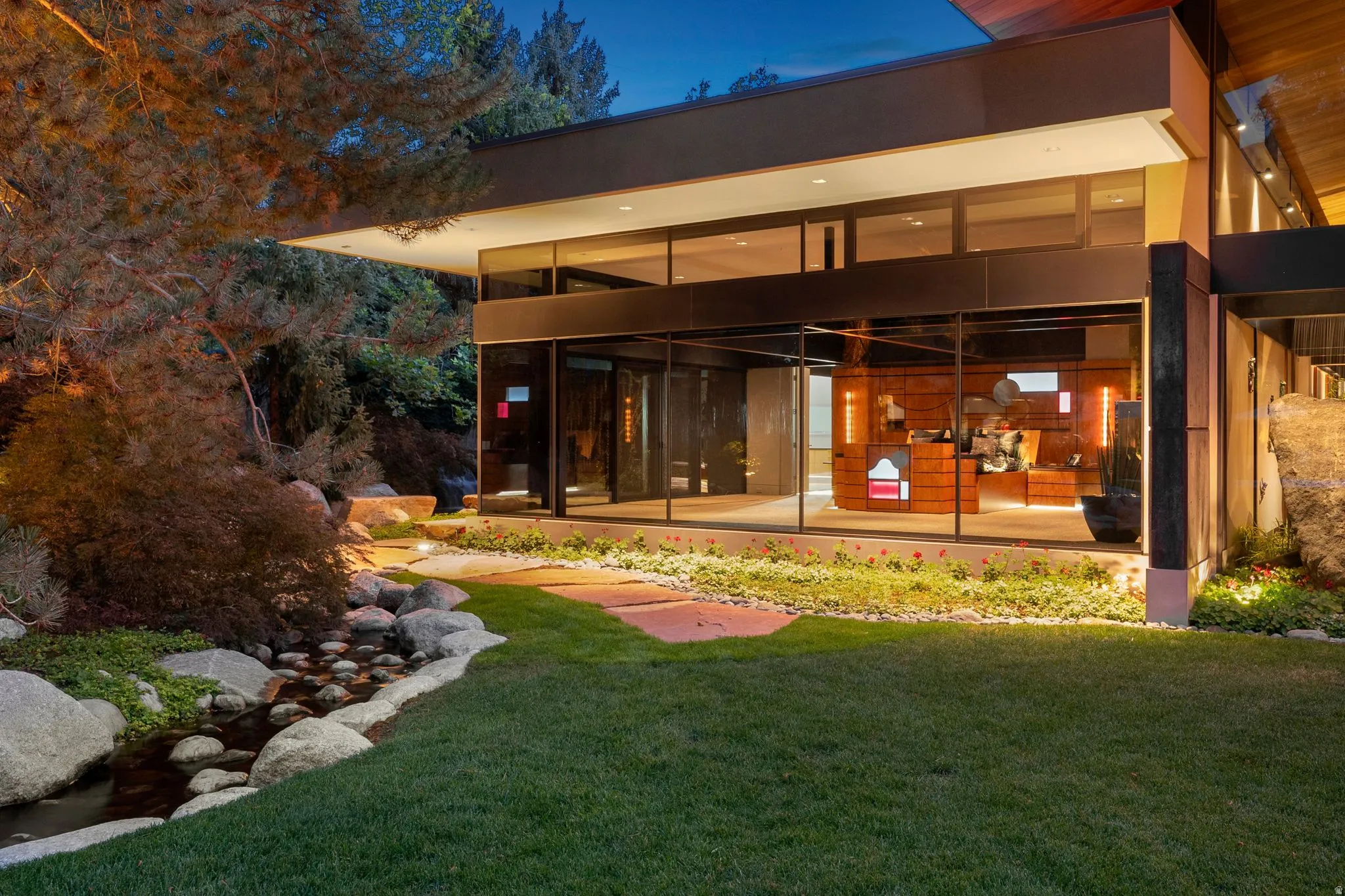 Modern architectural design featuring expansive glass walls, a manicured lawn, and a stone-lined water feature