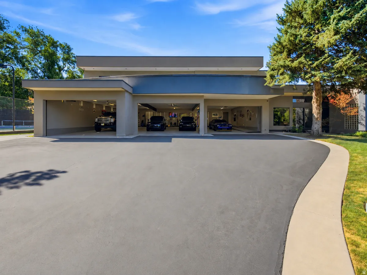 Contemporary exterior with multiple garage bays, expansive paved driveway, and mature landscaping