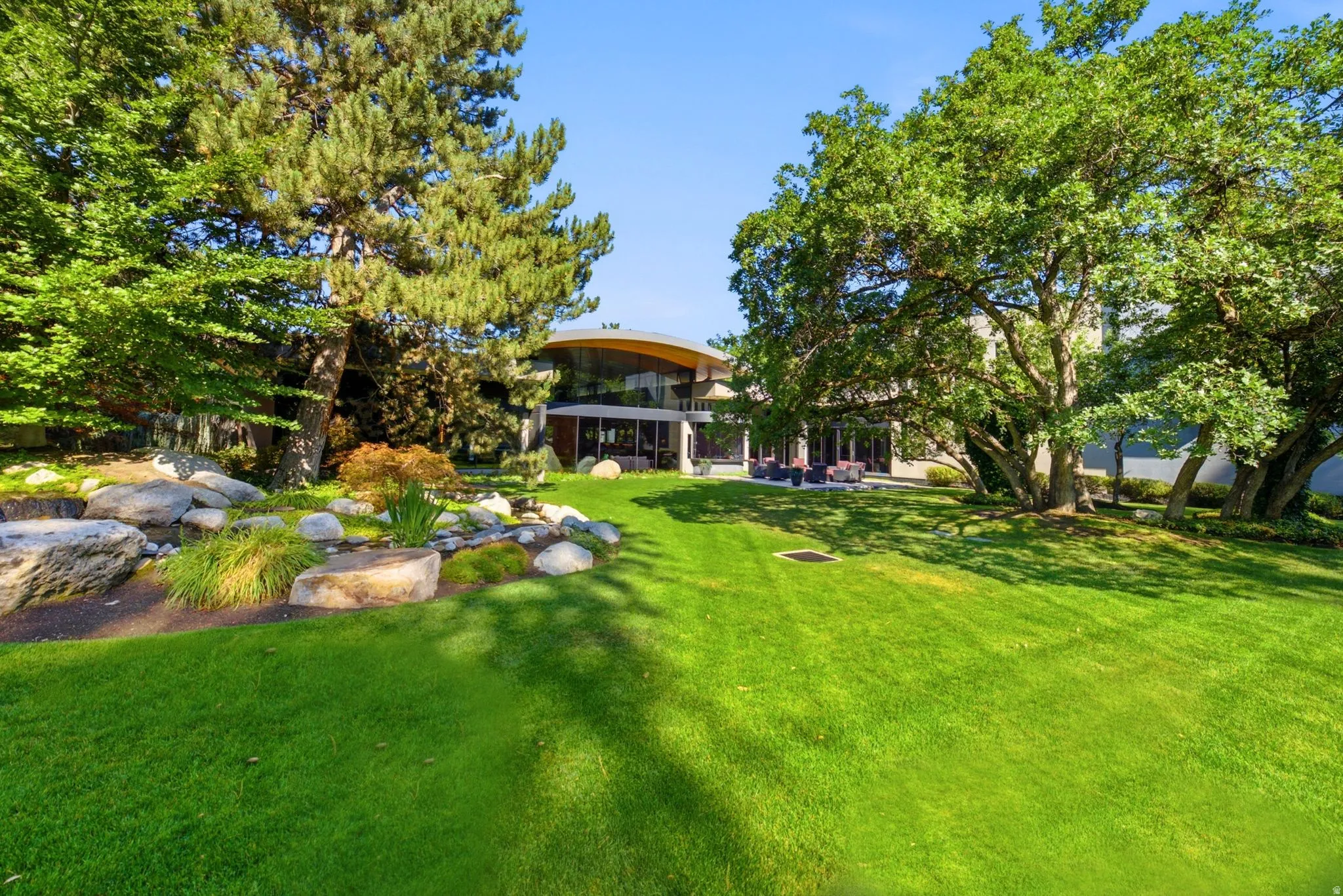 Expansive lawn with mature trees, a rock garden, and a curved architectural element
