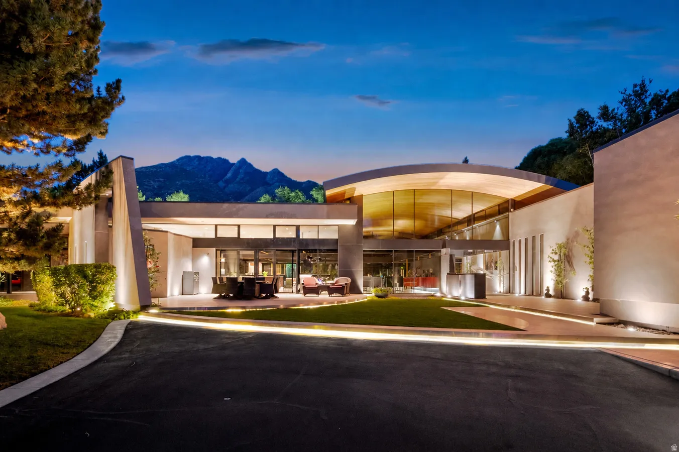 Modern architectural residence featuring extensive glass curtain walls, a curved roofline, and integrated outdoor lighting