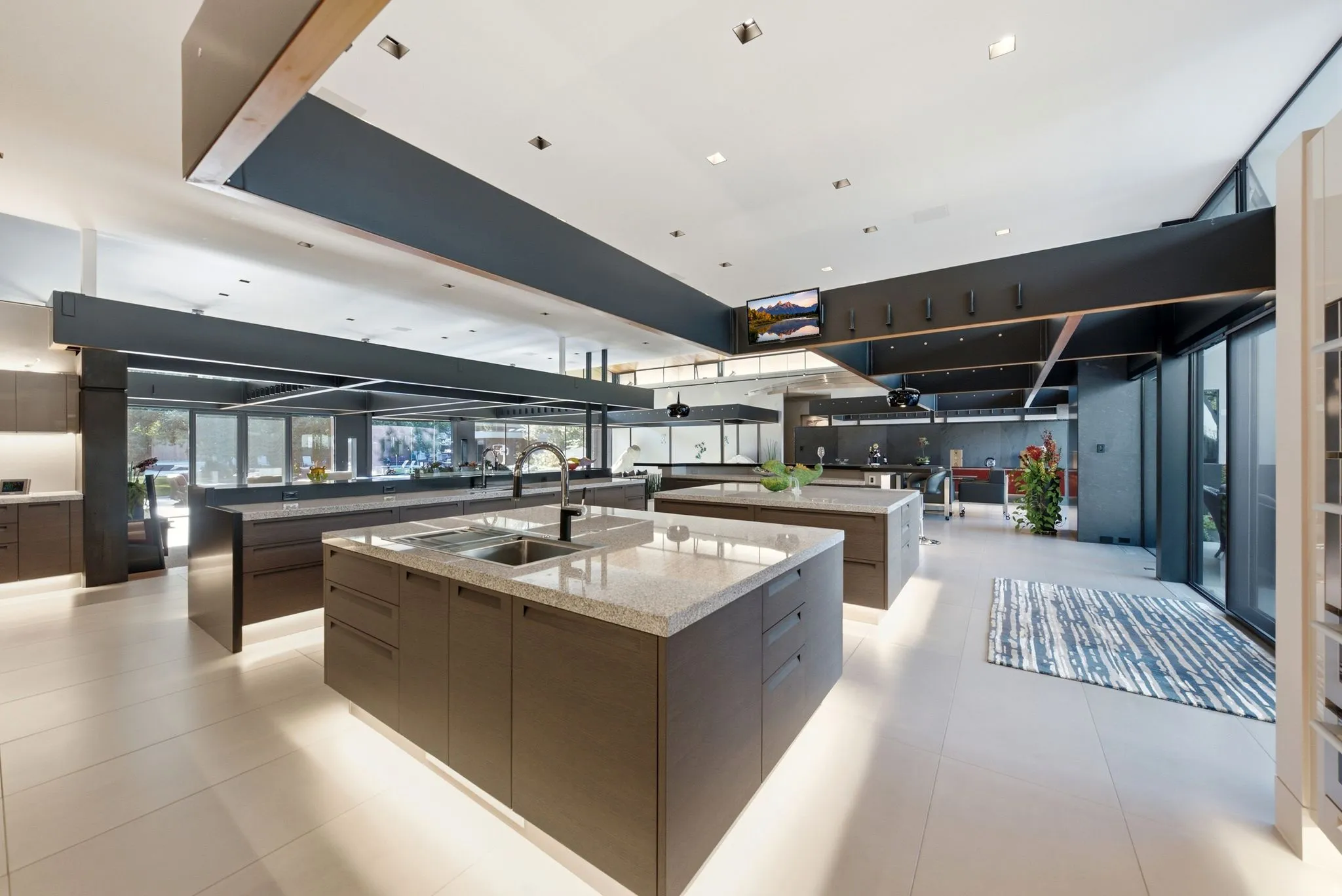 Expansive chef's kitchen featuring dual islands with light-honed stone countertops, dark cabinetry with integrated appliances, recessed and pendant lighting, and polished concrete flooring