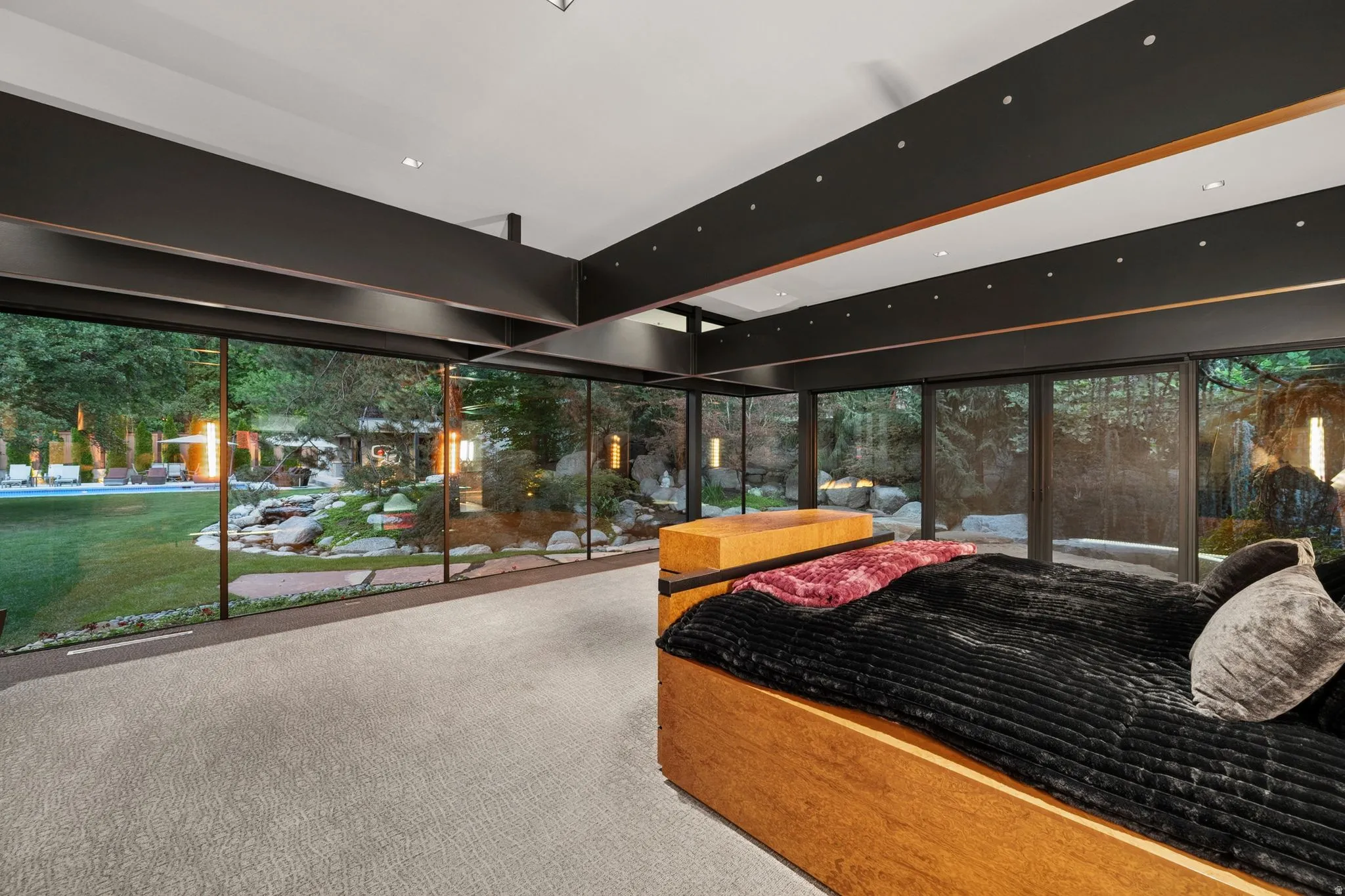 Floor-to-ceiling glass panels, outdoor landscaping, recessed ceiling lighting, and exposed structural beams