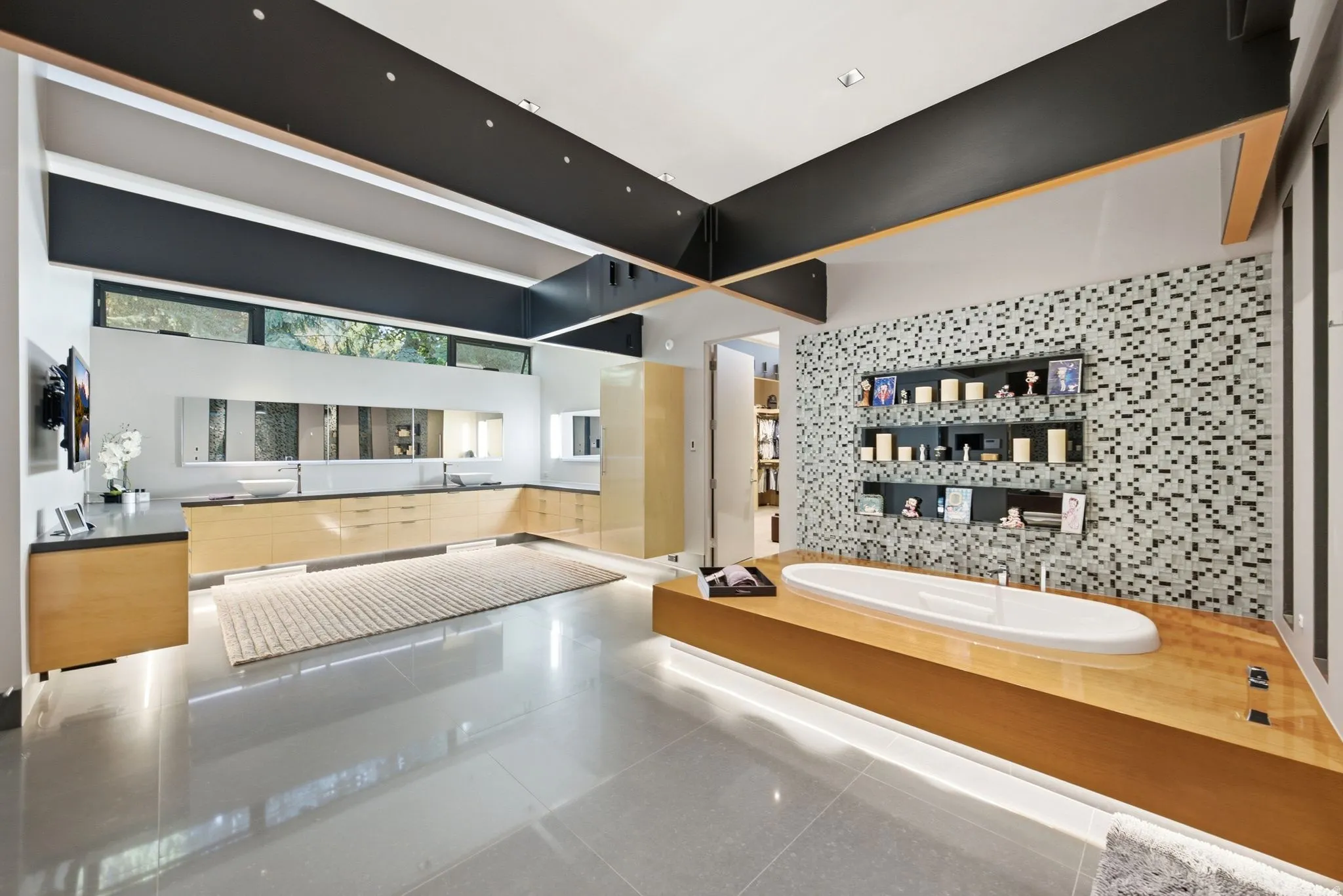 Expansive bathroom with a built-in soaking tub, full wall of mosaic tile, and a floating wood-finish vanity with dual vessel sinks