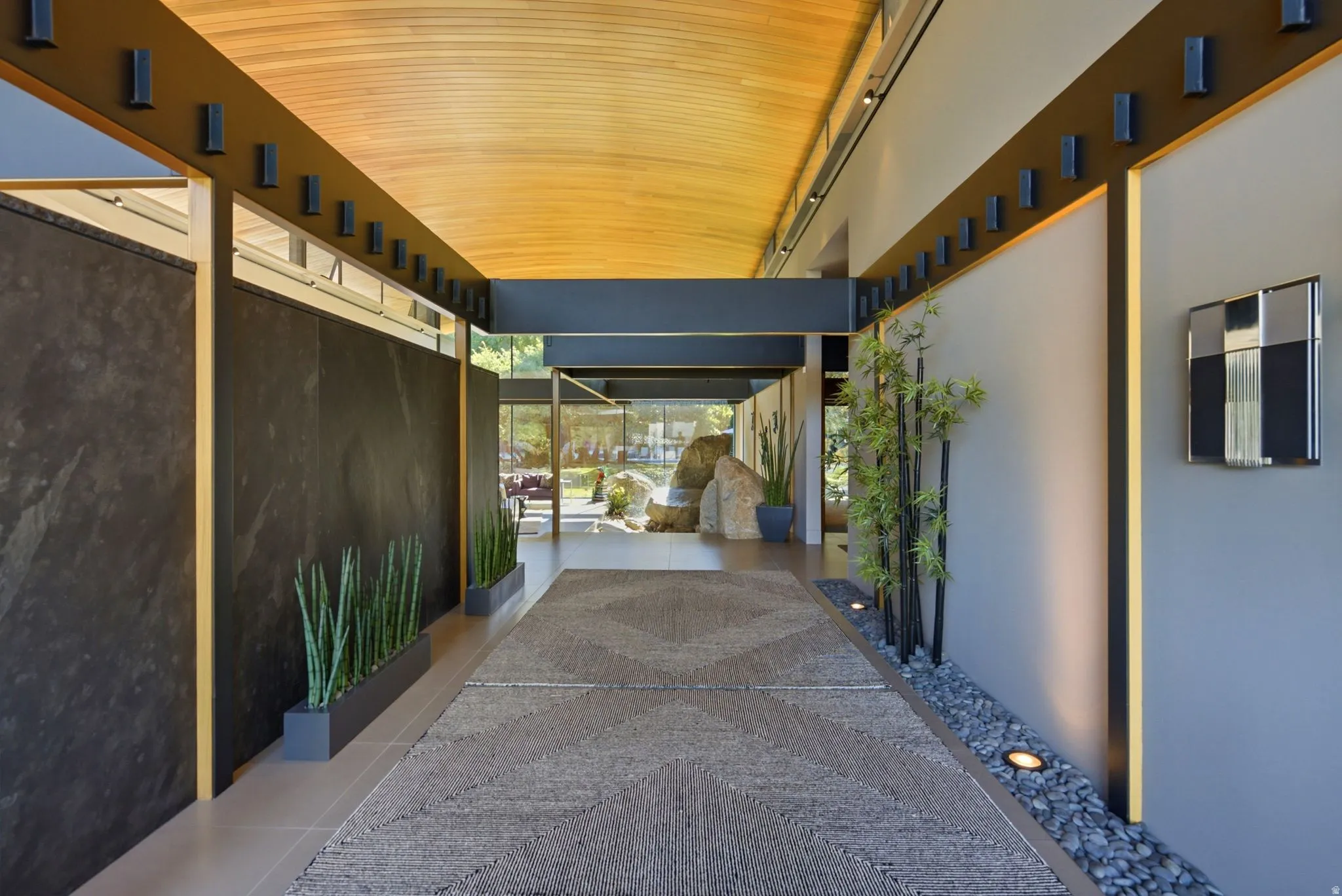 Covered exterior walkway featuring a wood-finish ceiling, exposed structural beams, and integrated lighting