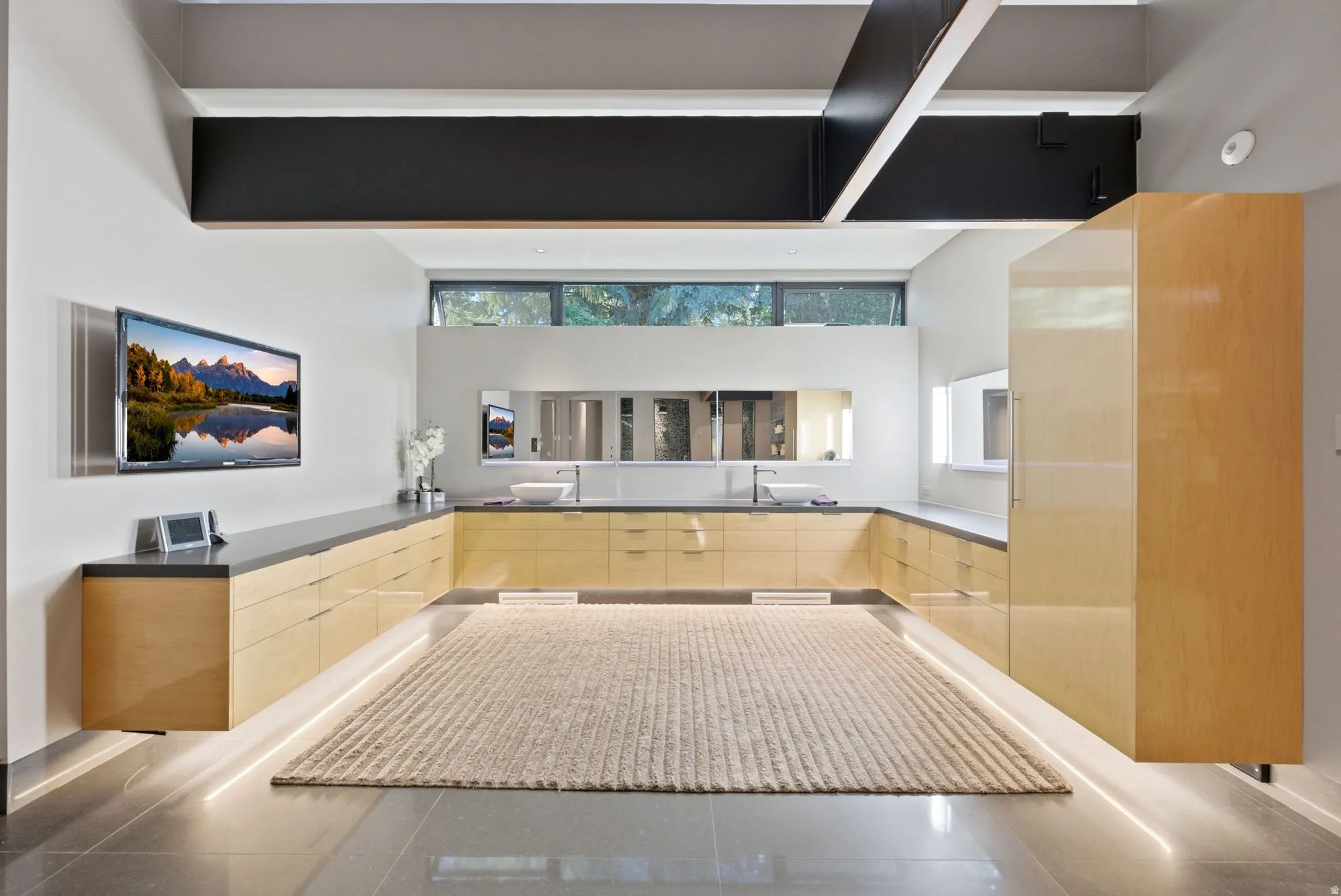 Floating wood-finish cabinetry with integrated lighting, dual vessel sinks, and large format tile flooring