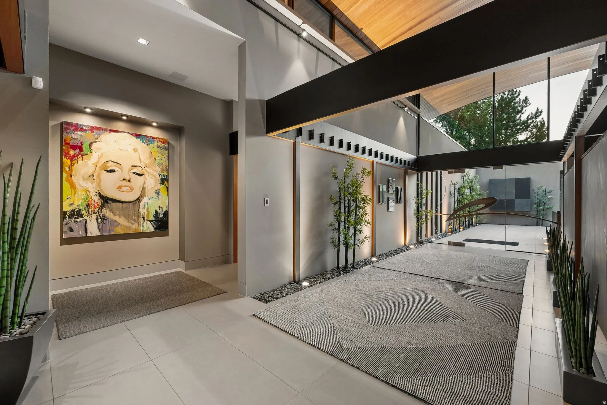 High ceilings with wood paneling, recessed lighting, expansive floor-to-ceiling glass, and a modern open staircase with glass railing