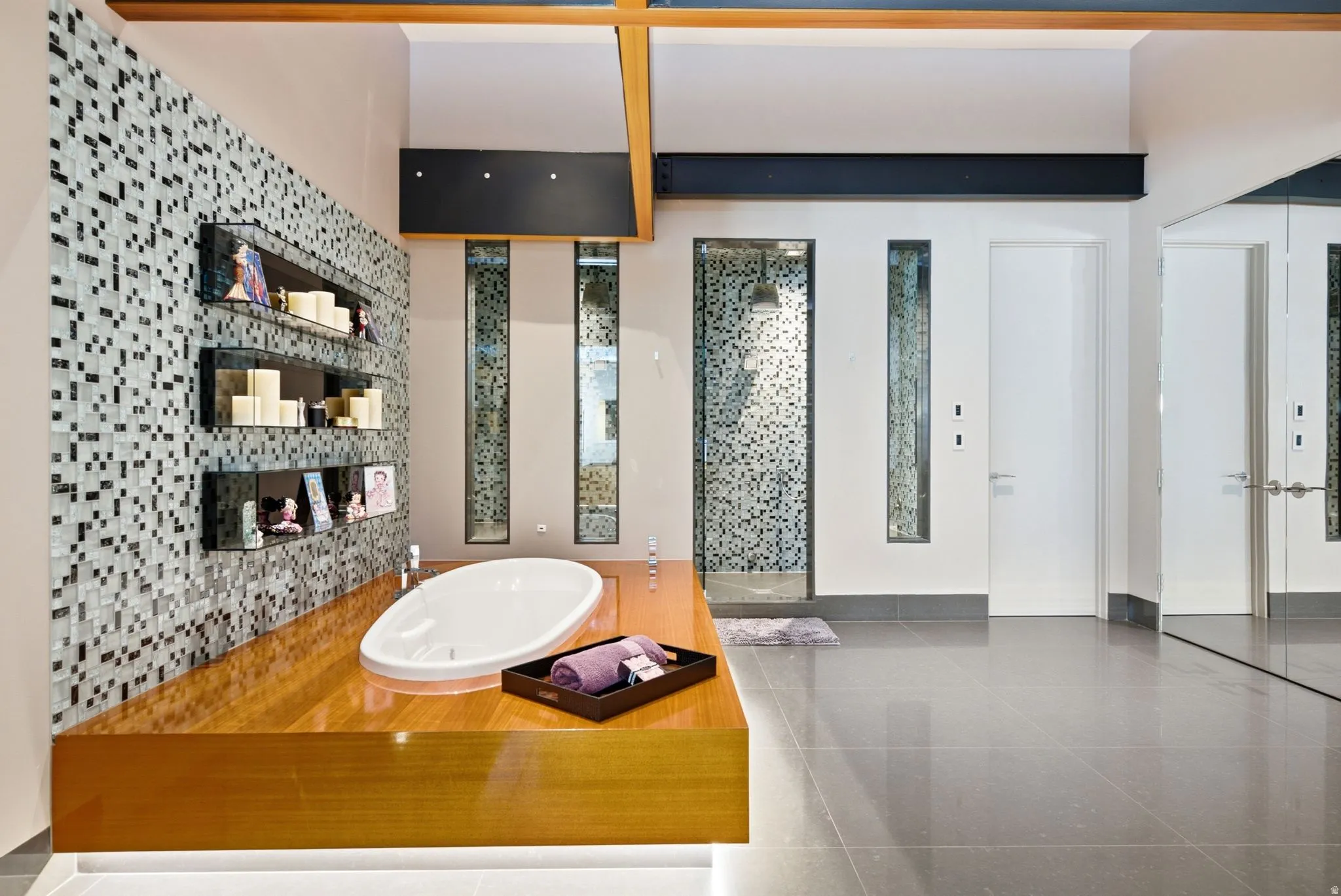 Large format tile flooring, built-in soaking tub, mosaic tile accent wall, glass-enclosed shower, and wood-finish countertop
