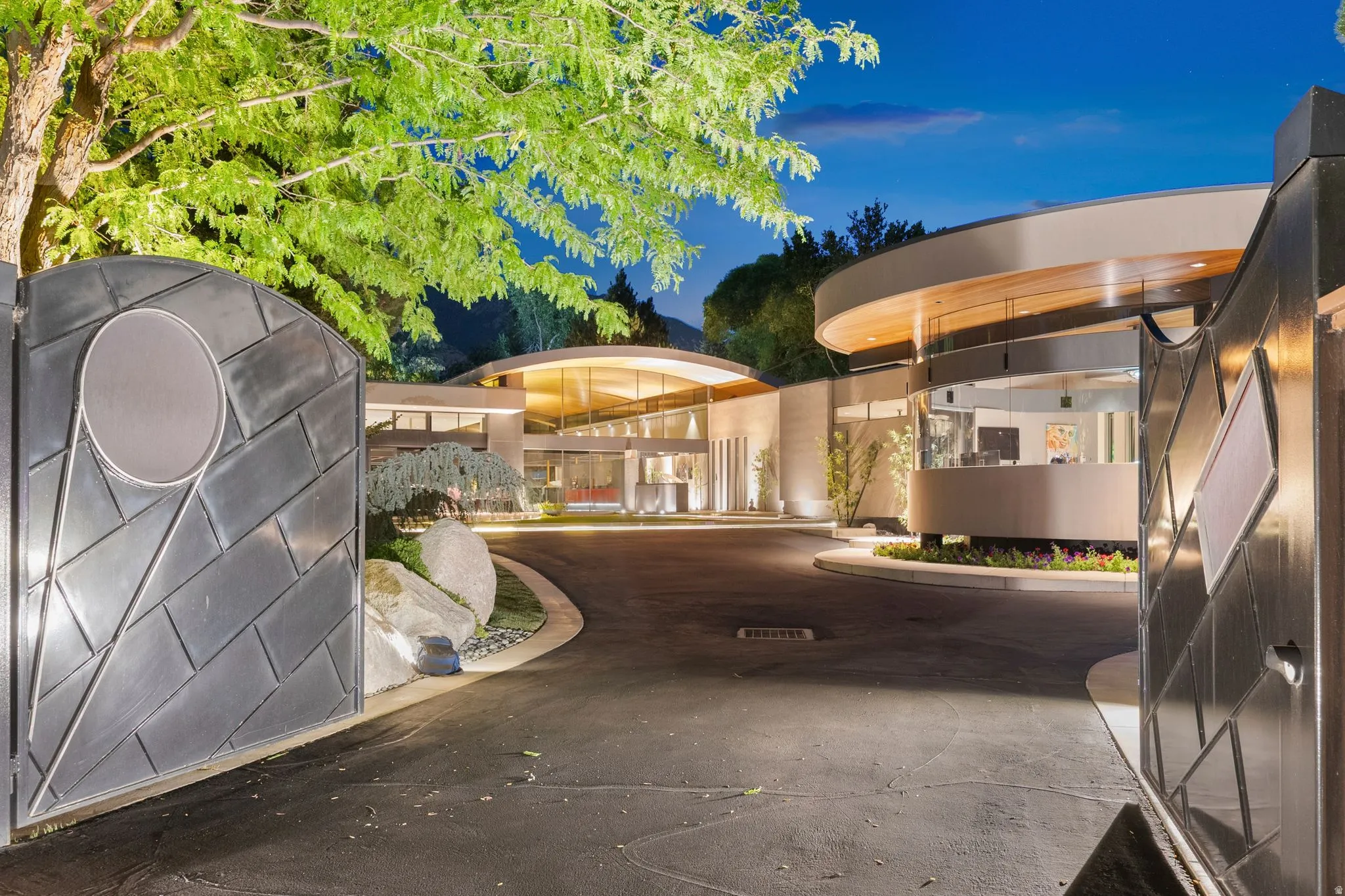 Contemporary architecture with expansive curved windows, a circular drive, and a custom gate