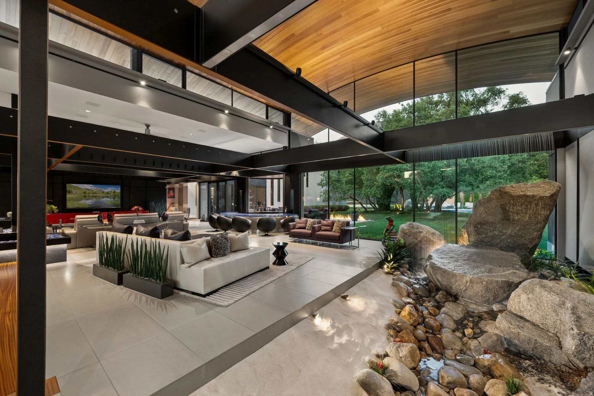 Open-concept living area with expansive glass walls, a wood-paneled vaulted ceiling, and exposed structural beams