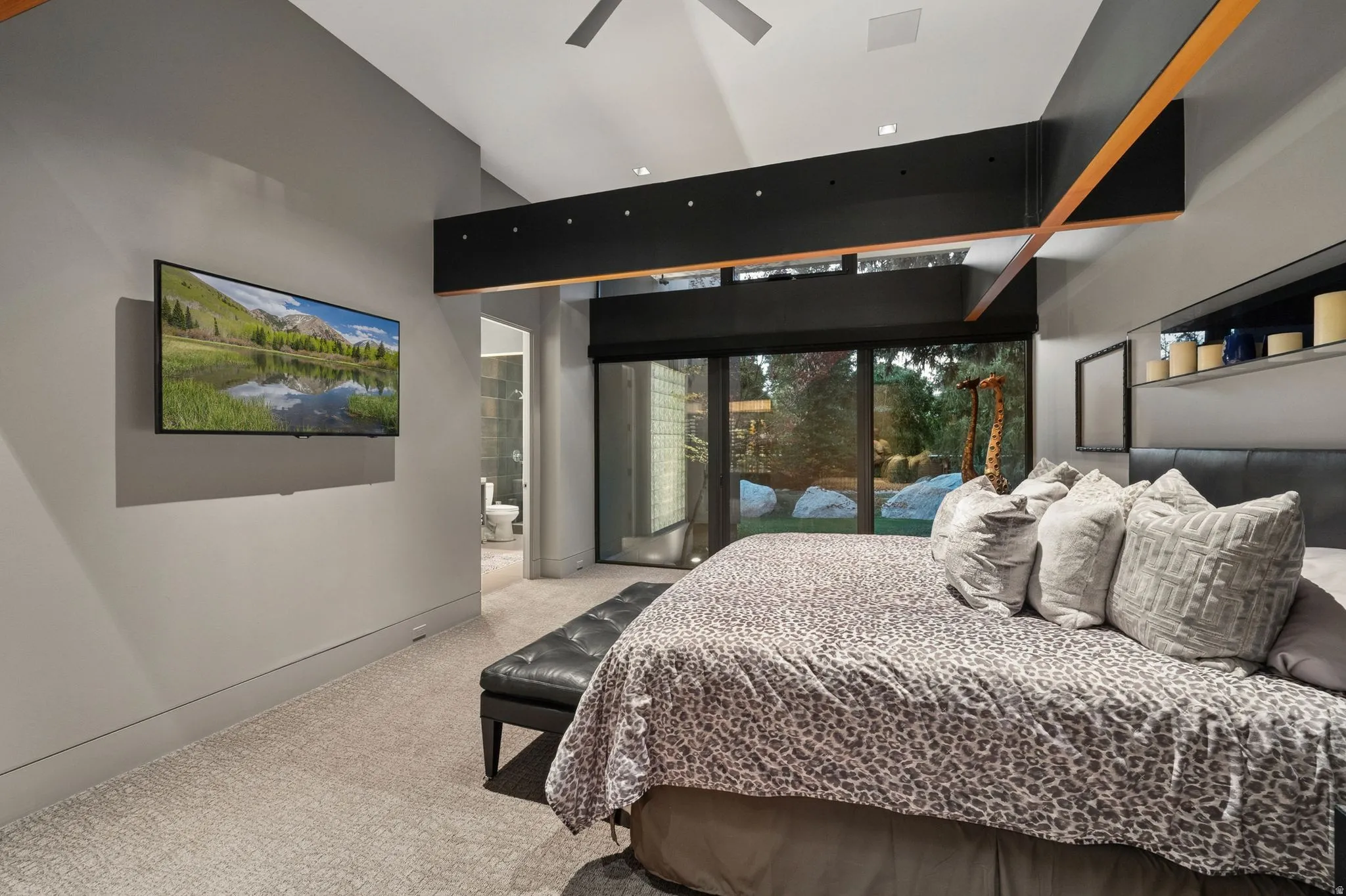 Vaulted ceiling with exposed wood beams, wall-mounted television, large sliding glass doors, built-in shelving, and recessed lighting