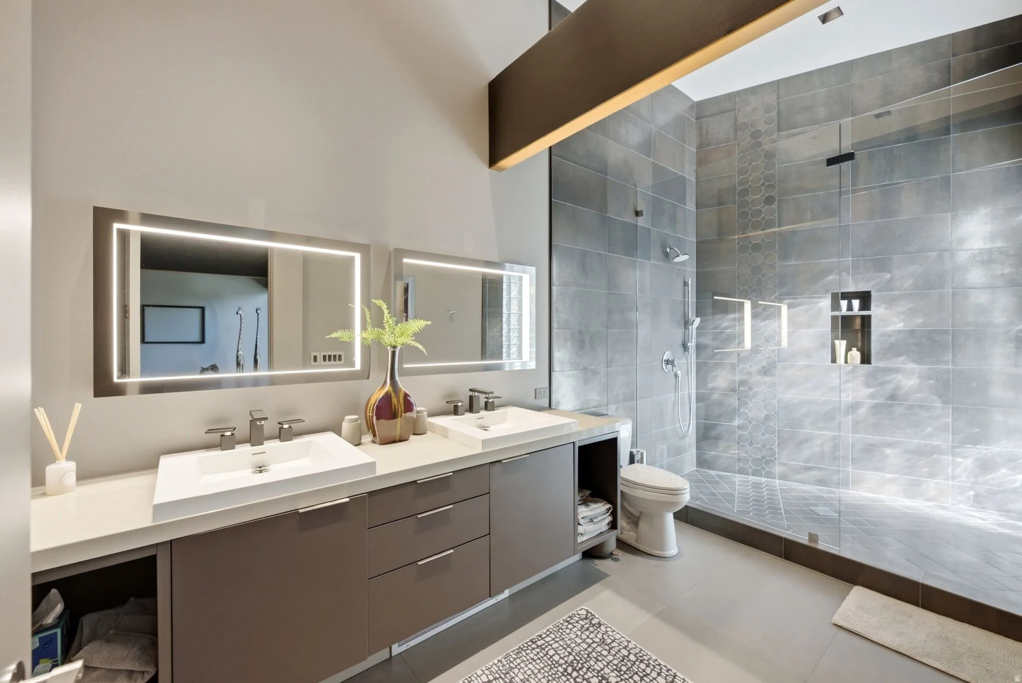 Dual vanity with integrated sinks, illuminated mirrors, a glass-enclosed shower with a rainfall showerhead, and a built-in shower niche