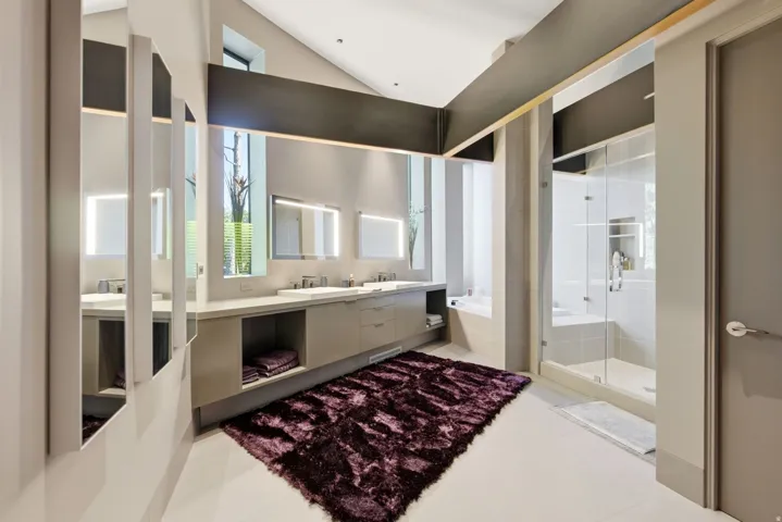 Vaulted ceiling with exposed beam, dual vanity with undermount sinks, frameless glass shower enclosure, built-in shower bench, and a standalone soaking tub