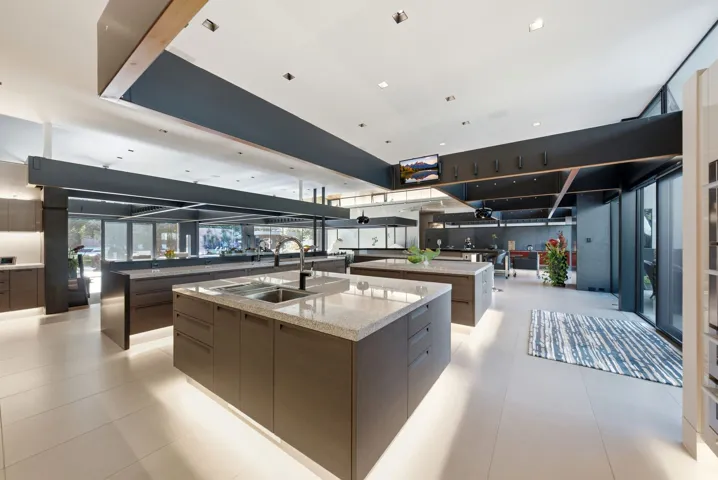 Expansive chef's kitchen featuring dual islands with light-honed stone countertops, dark cabinetry with integrated appliances, recessed and pendant lighting, and polished concrete flooring