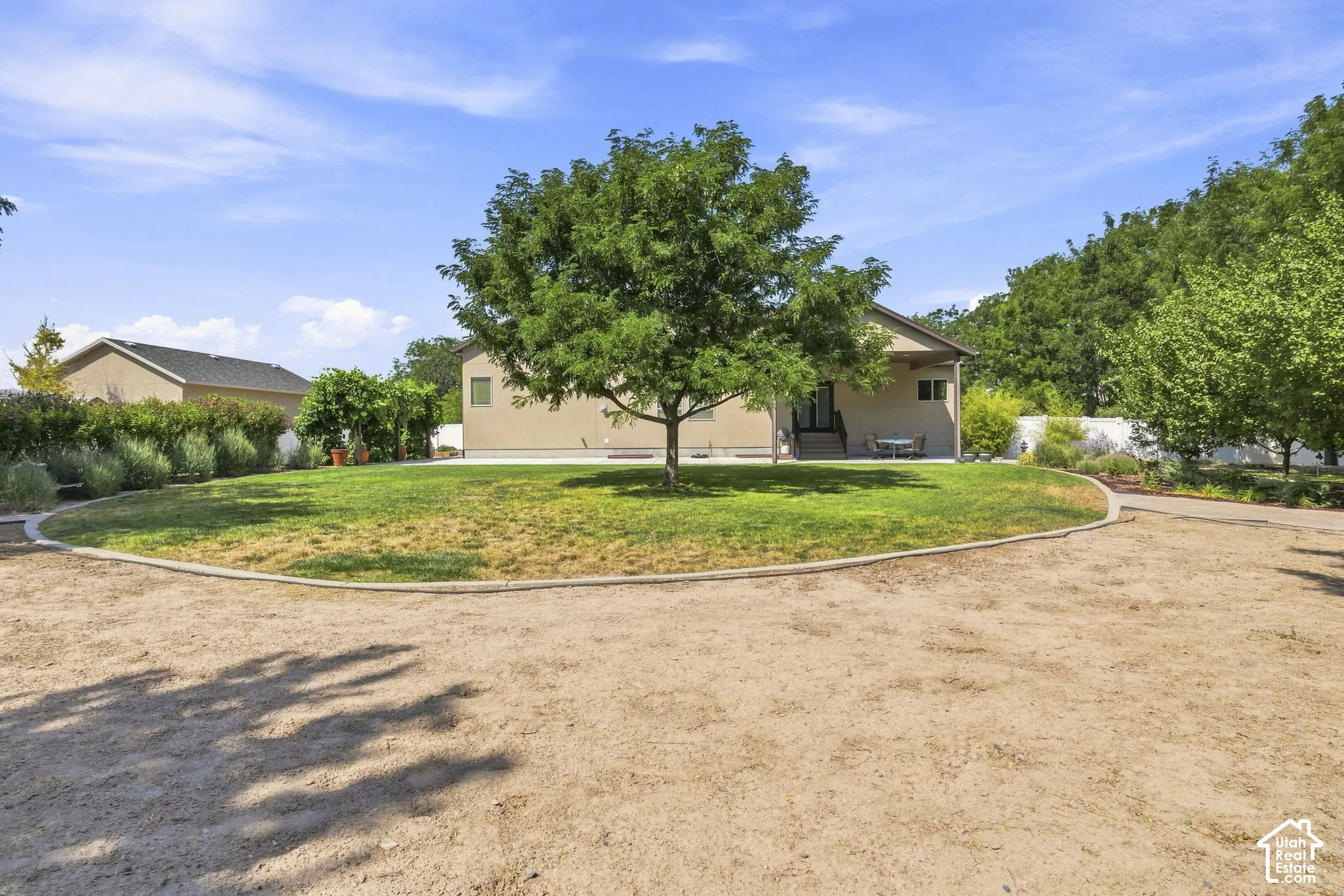 Expansive gravel parking area with a defined border, leading to a sprawling lawn featuring a mature shade tree