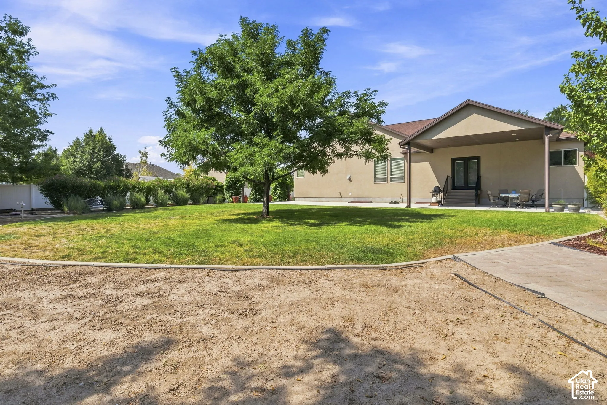 Expansive green lawn with mature trees, stucco exterior, covered patio, and concrete pathway