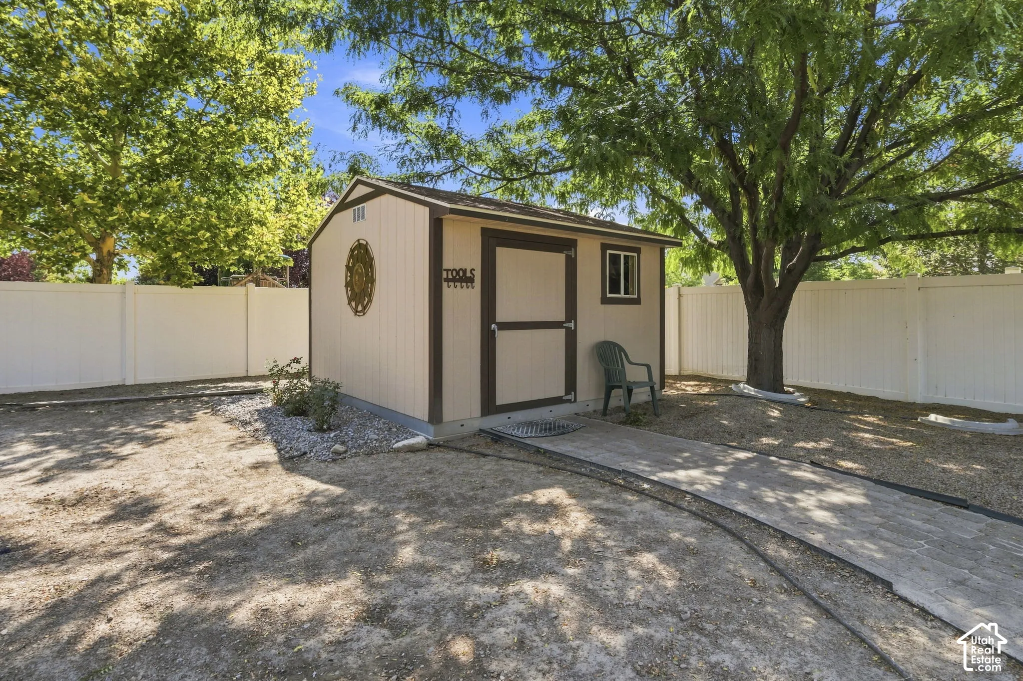Detached shed with an exterior window and wood-look door, complemented by a white privacy fence and mature tree