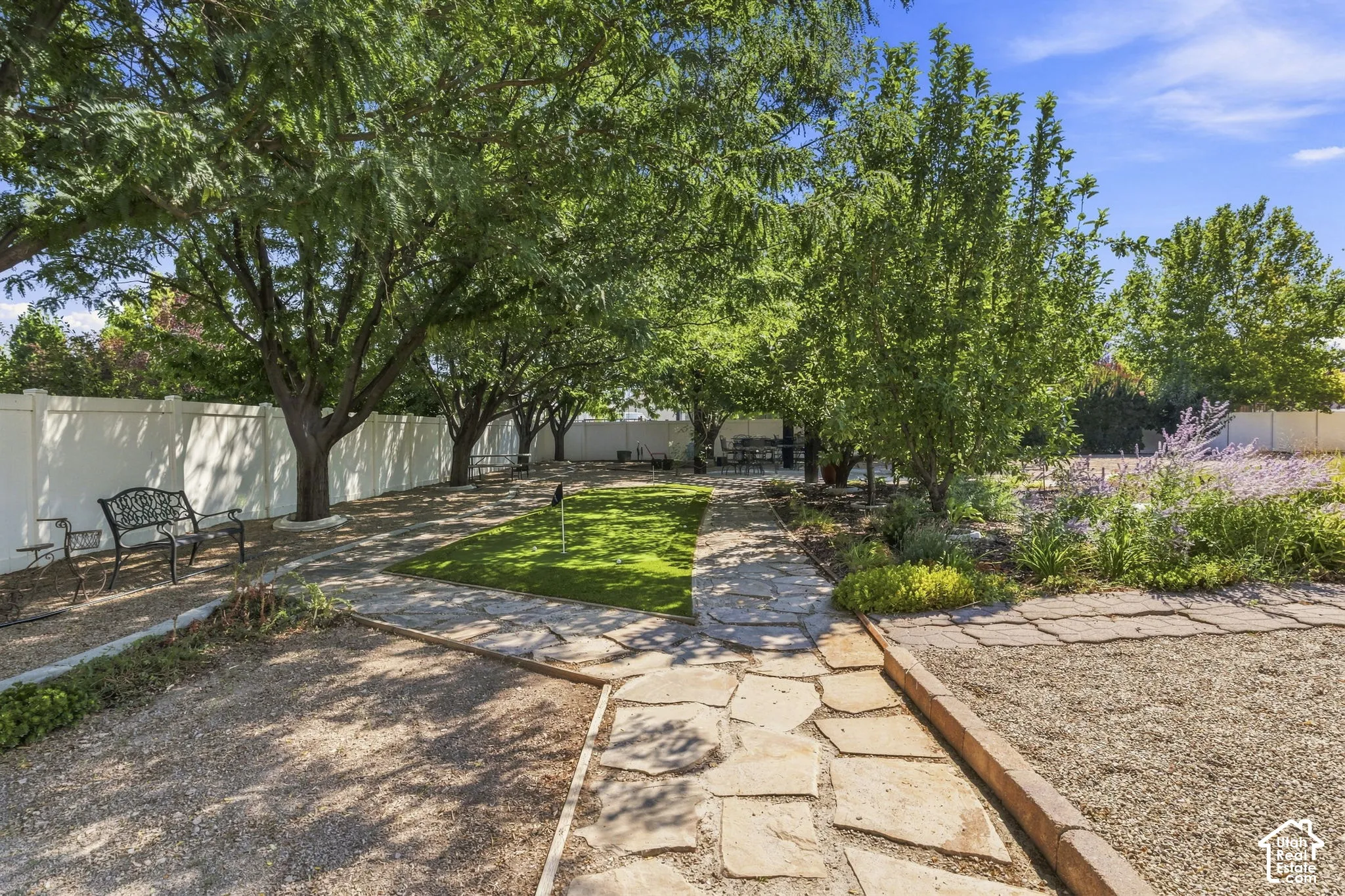 Expansive backyard featuring mature trees, a manicured lawn, flagstone pathways, gravel landscaping, and a privacy fence