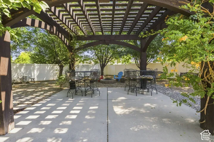 Expansive concrete patio with a dark wood pergola, gravel landscaping, and a white privacy fence