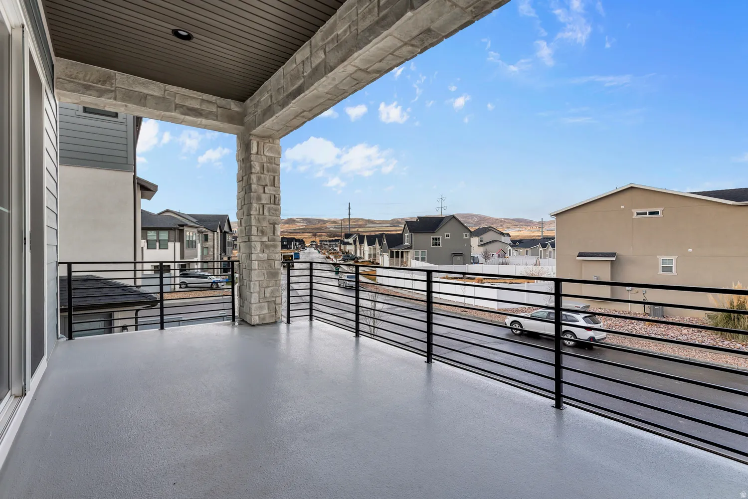 Expansive covered balcony featuring a stone pillar, black metal railing, and wood-finish soffit