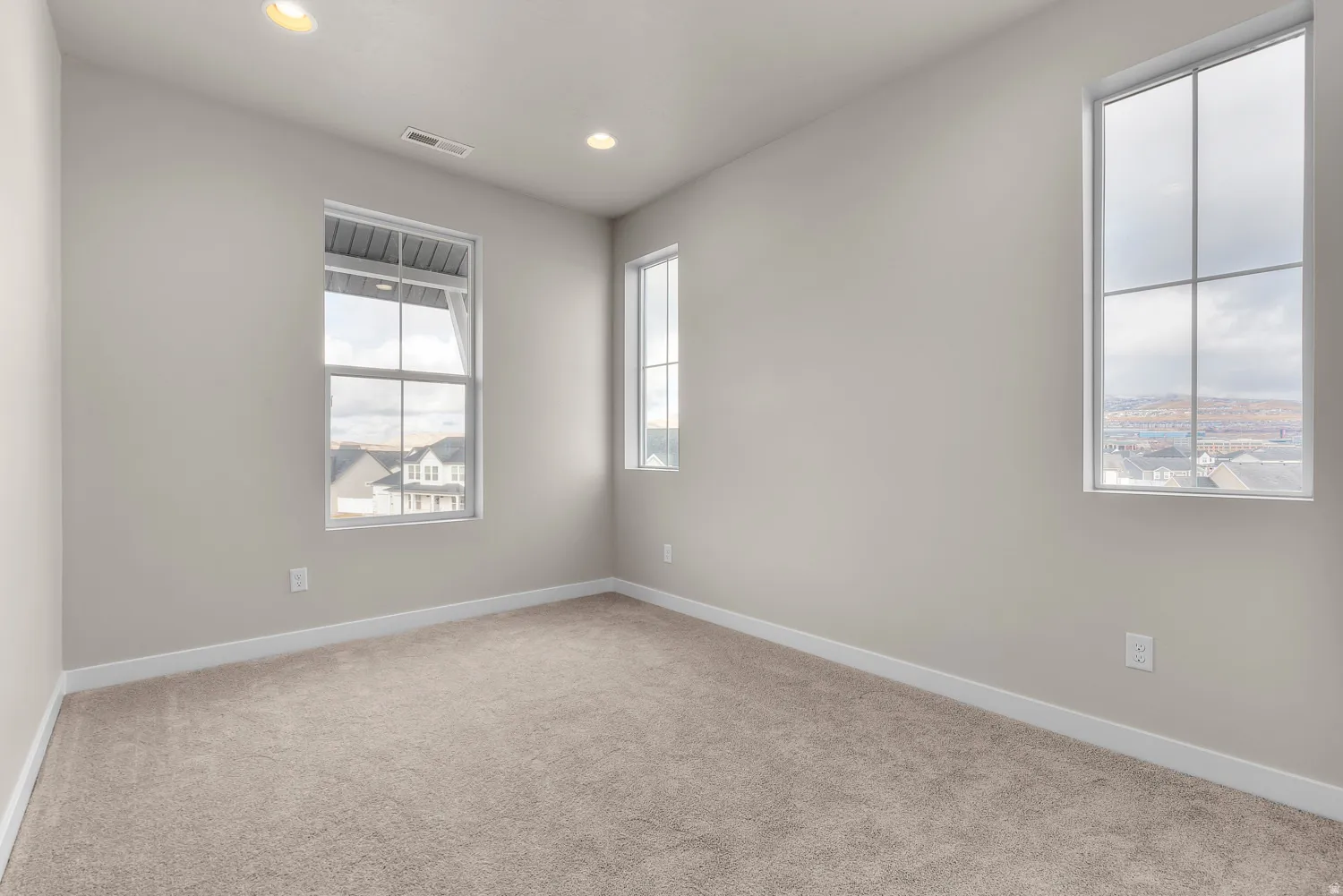 Neutral tone wall finish, recessed ceiling lighting, light beige carpeting, multiple windows, and white trim