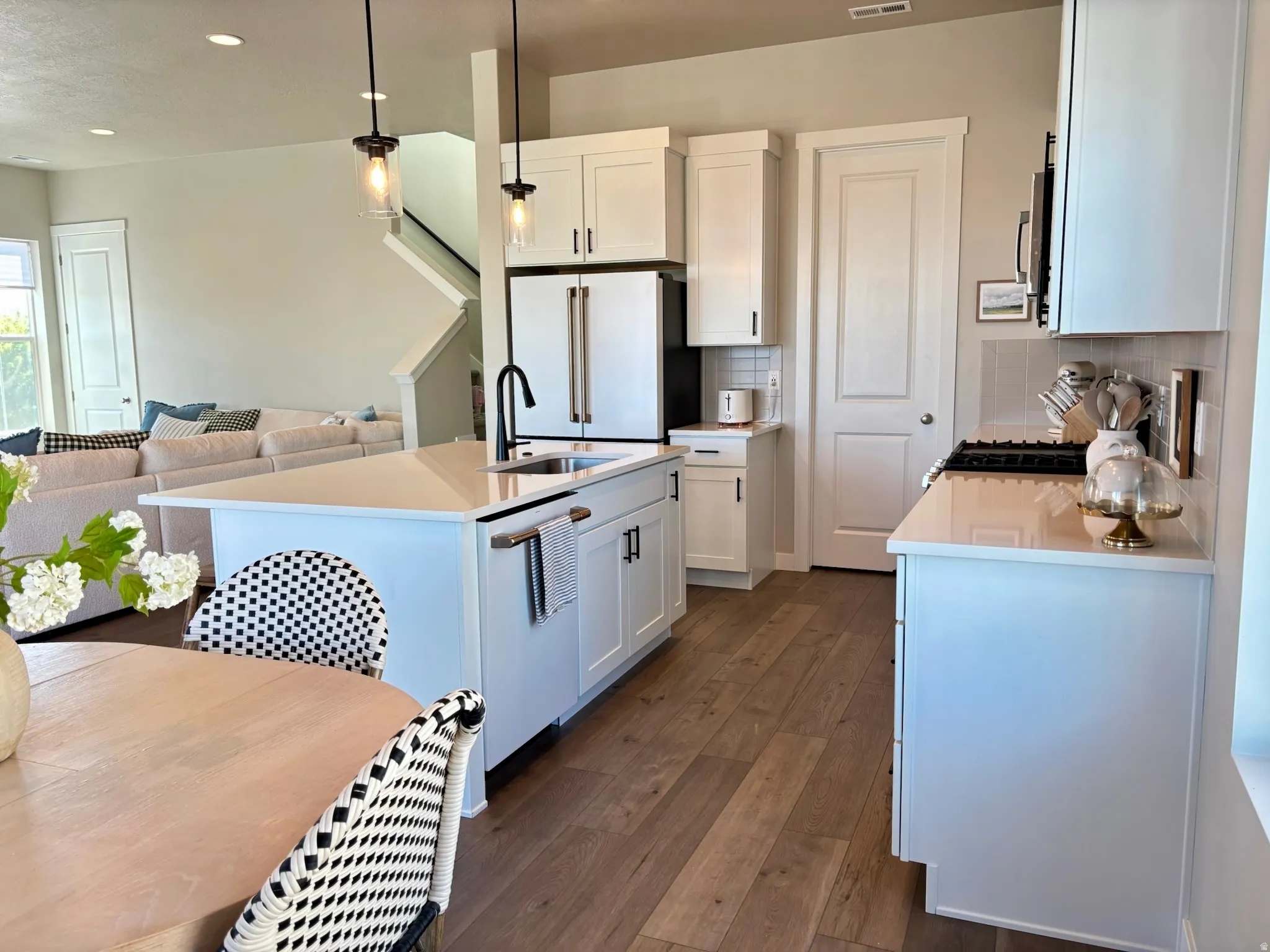 Kitchen featuring wood-finish flooring, white cabinetry, a central island with a sink, and pendant lighting