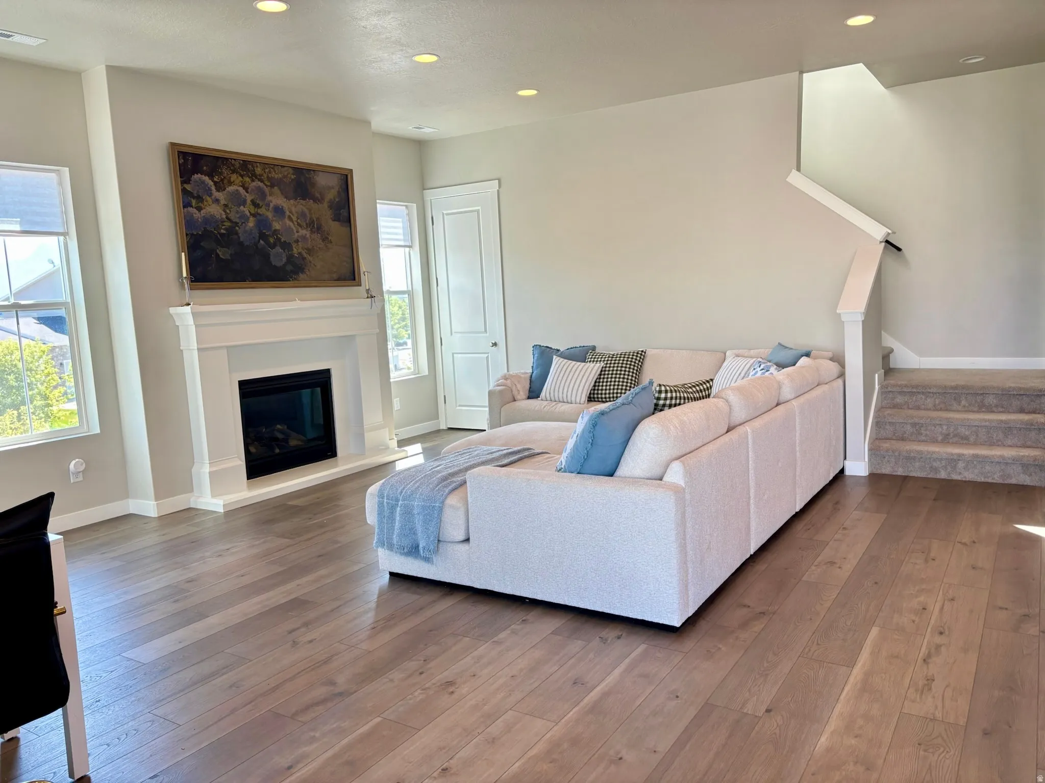 Wood-finish flooring, recessed lighting, and a modern fireplace with a white mantel