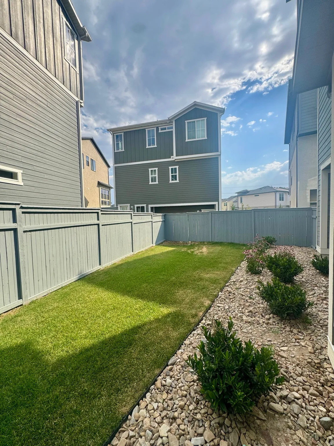 Enclosed yard featuring a manicured lawn, a rock landscaping bed, and mature shrubs