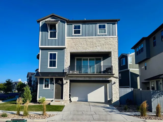 Modern two-story residence featuring a mixed-material exterior with stone and fiber cement siding, multi-pane windows, and a front-facing garage