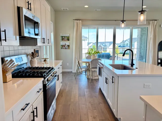 Gourmet kitchen featuring white cabinetry, stainless steel appliances, light-toned countertops, and wood-finish flooring