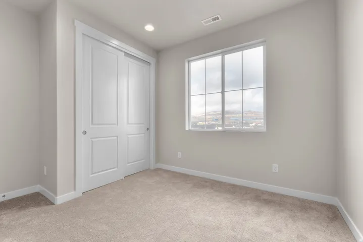 Recessed ceiling lighting, neutral tone carpeting, double sliding closet doors, and a multi-pane window